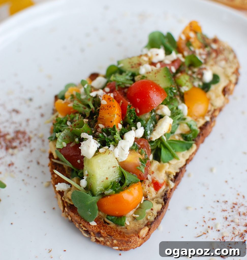 Single Slice of Hummus Toast A single slice of Mediterranean Hummus Toast with Za'atar, showcasing layers of hummus, fresh vegetables, and feta.