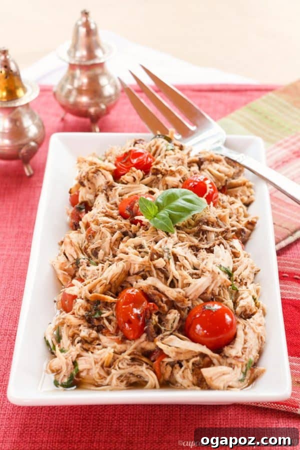 Juicy Slow Cooker Tomato Basil Pulled Chicken, shredded and mixed in a vibrant red sauce, garnished with fresh basil leaves.