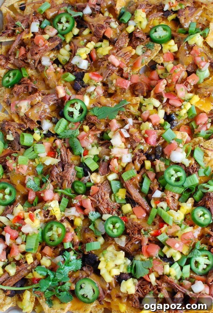 Ultimate Beef Nacho Platter 4 A sheet pan of partially assembled Beef Nachos, with a layer of tortilla chips, shredded beef, black beans, and cheese, ready to be baked.