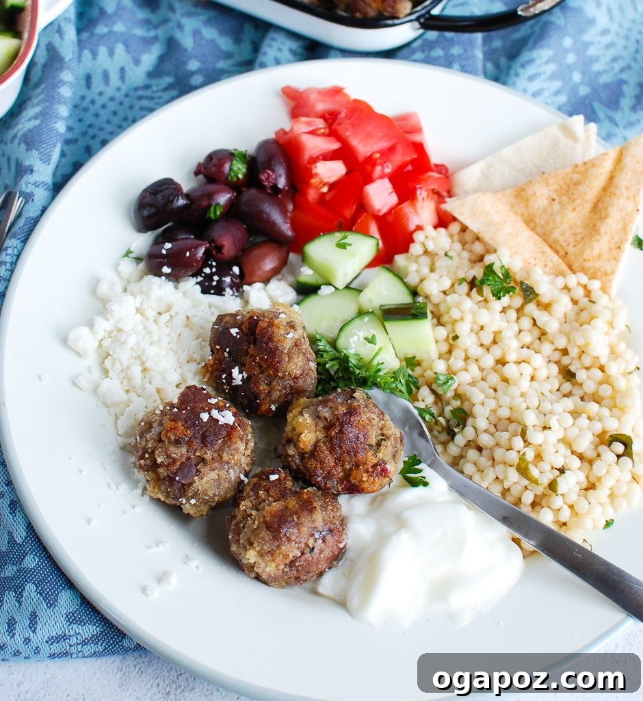 Authentic Greek Keftedes 4 Greek Meatballs served with warm pita bread, fresh cucumber, and tomato salad on a plate.