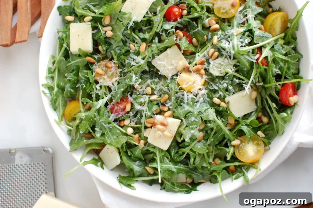 A bowl of Lemon Arugula Salad with Pine Nuts and Parmesan cheese, ready to be tossed.