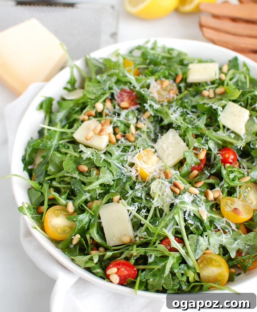 Lemon Arugula Salad with Pine Nuts being served with wooden tongs.