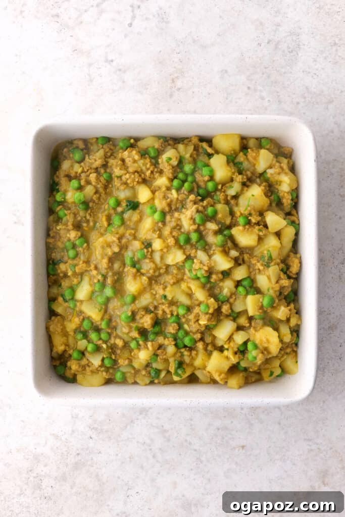 Carefully transferring the perfectly cooked samosa pie filling mixture into the baking pan, ready for its crust