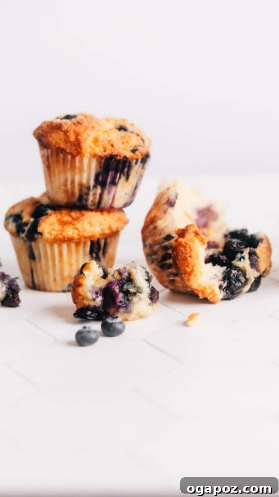 Blueberry Lemon Sour Cream Muffins 2 Stack of perfectly baked lemon blueberry sour cream muffins with one muffin halved, revealing juicy blueberries and a tender, moist crumb, on a rustic wooden table.