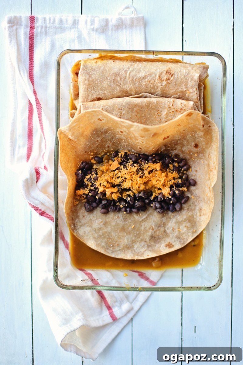 Fiery Pumpkin Black Bean Enchiladas 4 A close-up shot of hands assembling black bean and cheese enchiladas, rolling them in flour tortillas.