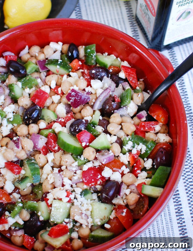 A generously filled bowl of Greek Chickpea Salad, bursting with fresh vegetables like cucumbers and tomatoes, along with chickpeas and crumbled feta.