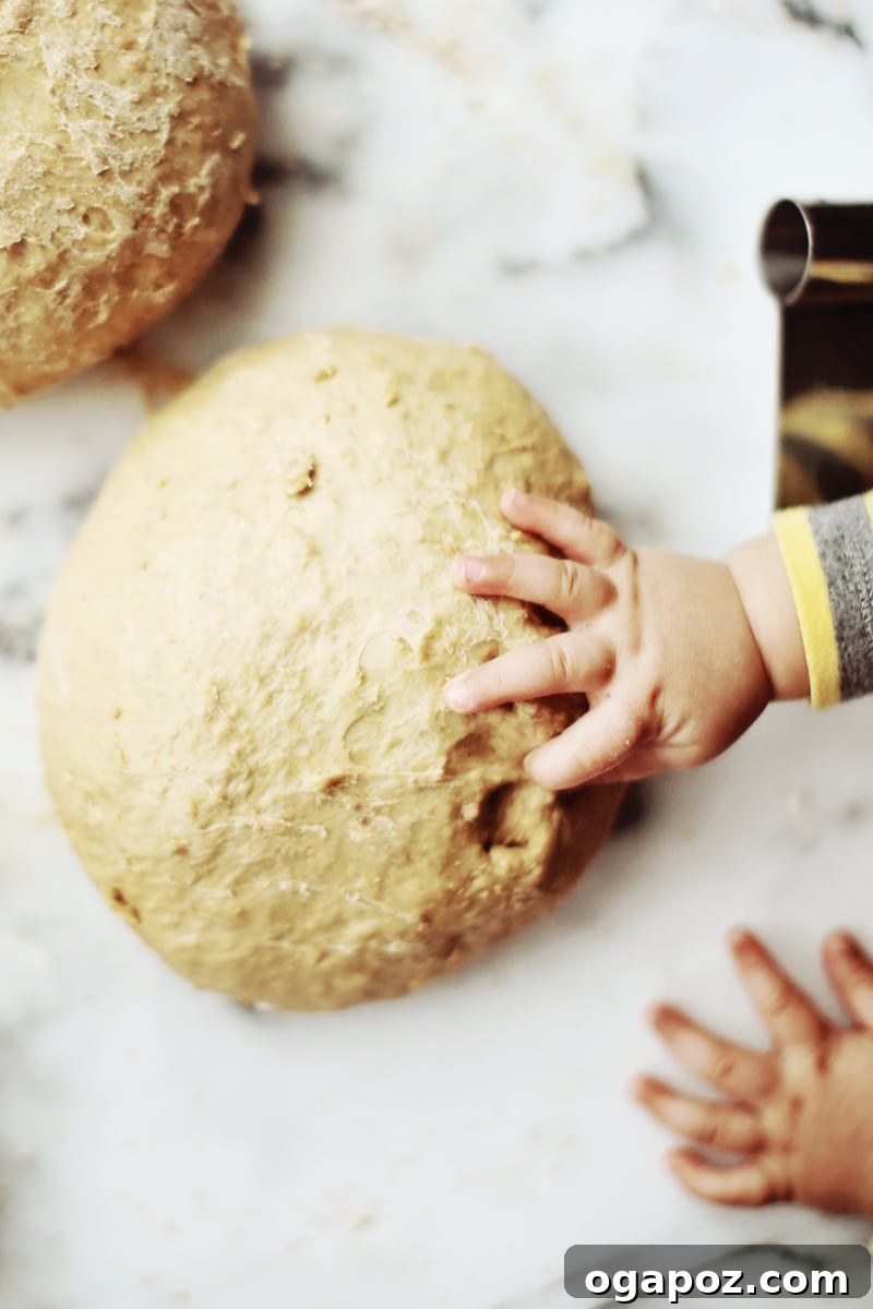 A child's finger pressing firmly into a risen bread dough loaf on a baking sheet, demonstrating a readiness test.