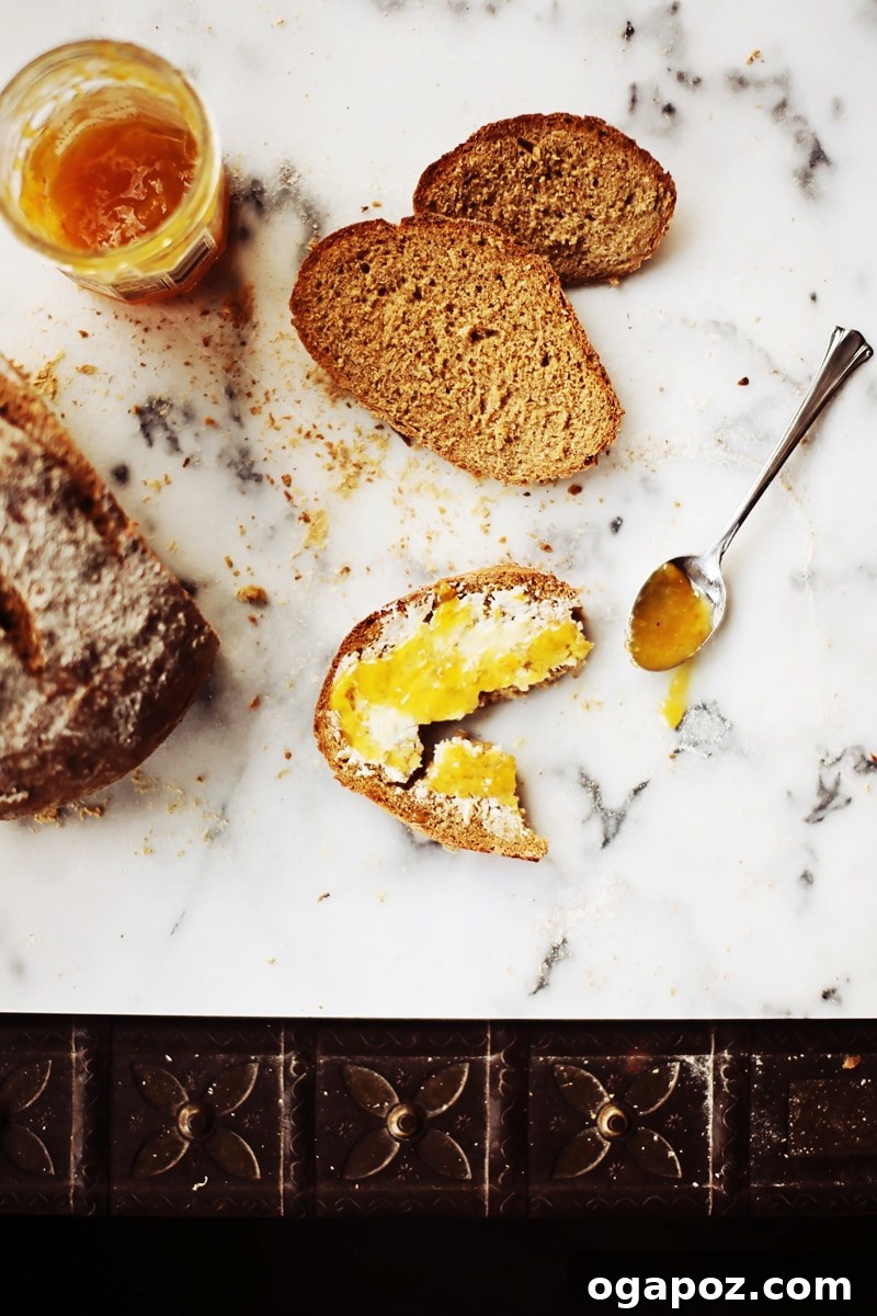 A rustic arrangement of golden brown oatmeal brown bread slices, butter, and a jar of vibrant orange marmalade on a wooden board.