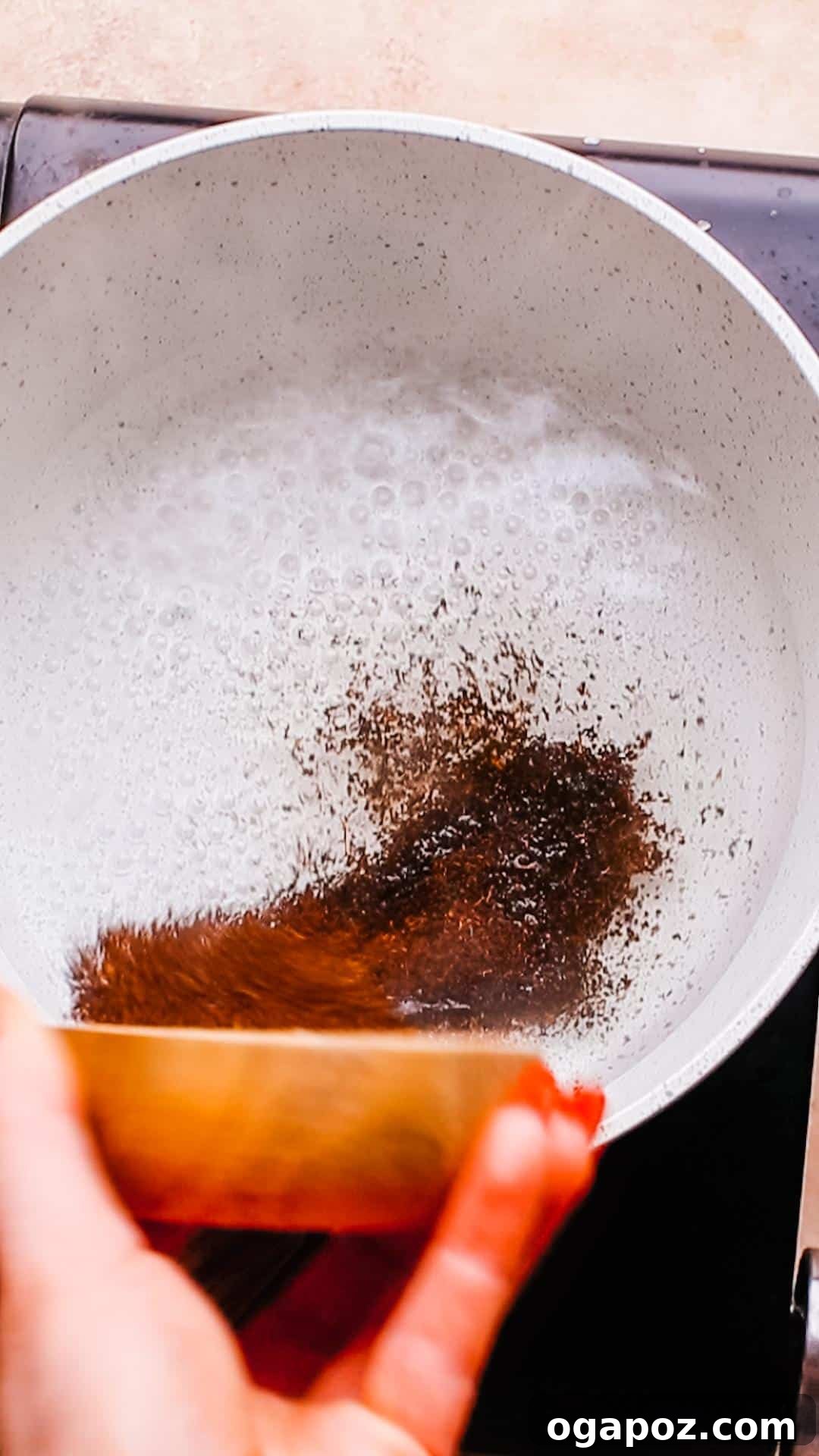 Authentic Karak Chai Made Simple 6 Black tea and spices being added to boiling water in a saucepan for Karak Chai.