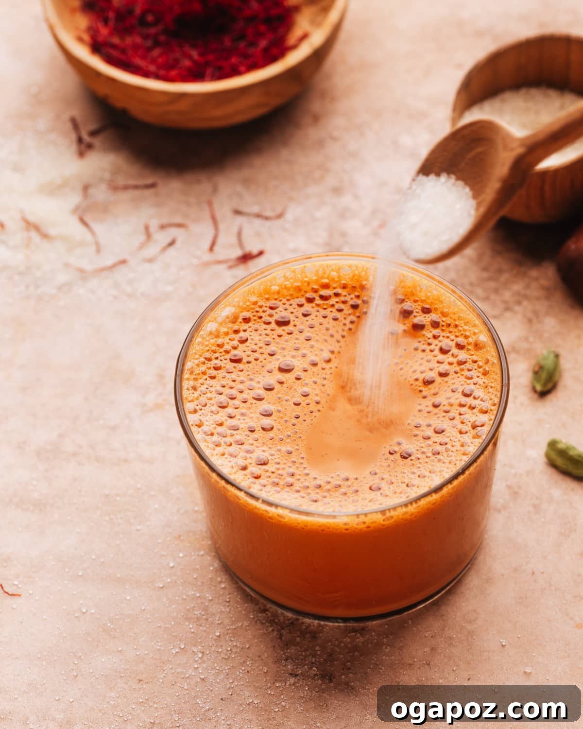 Authentic Karak Chai Made Simple 9 Adding a spoonful of sugar to a glass of Karak Chai, ready to be stirred and enjoyed.