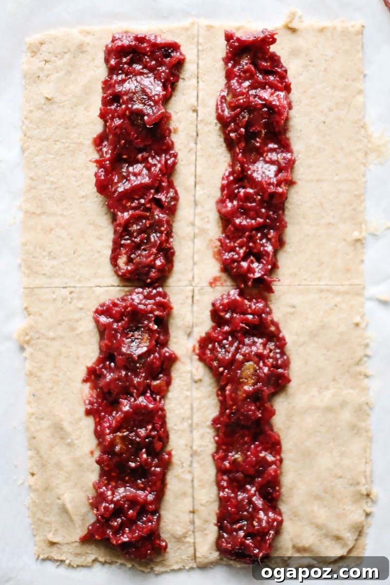 A close-up view of the whole wheat dough rolled out between parchment paper, alongside a bowl of the vibrant date and raspberry filling, ready for assembly.