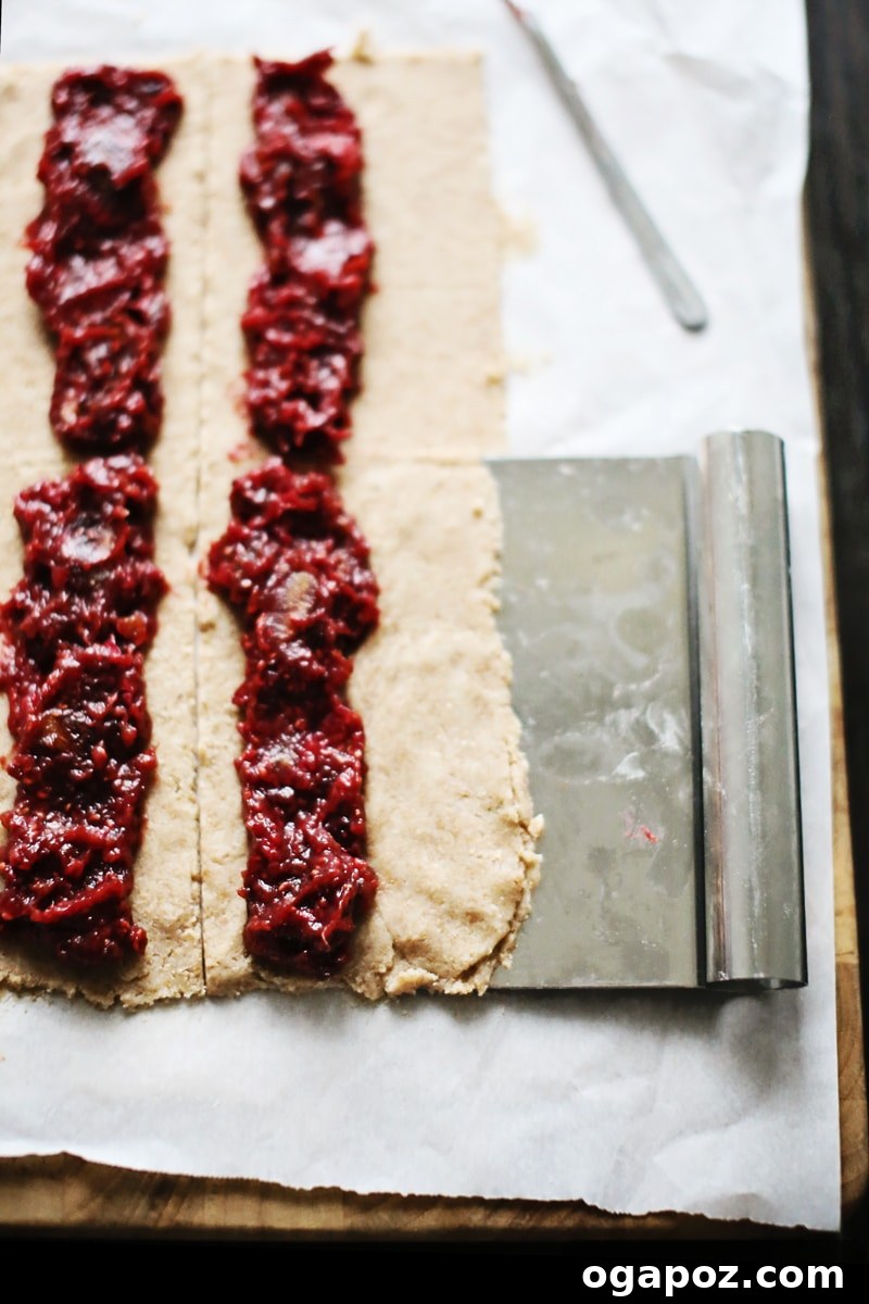 A close-up of partially assembled fig bars on parchment paper, showing the fruit filling carefully placed along the dough strips, ready for folding and baking.