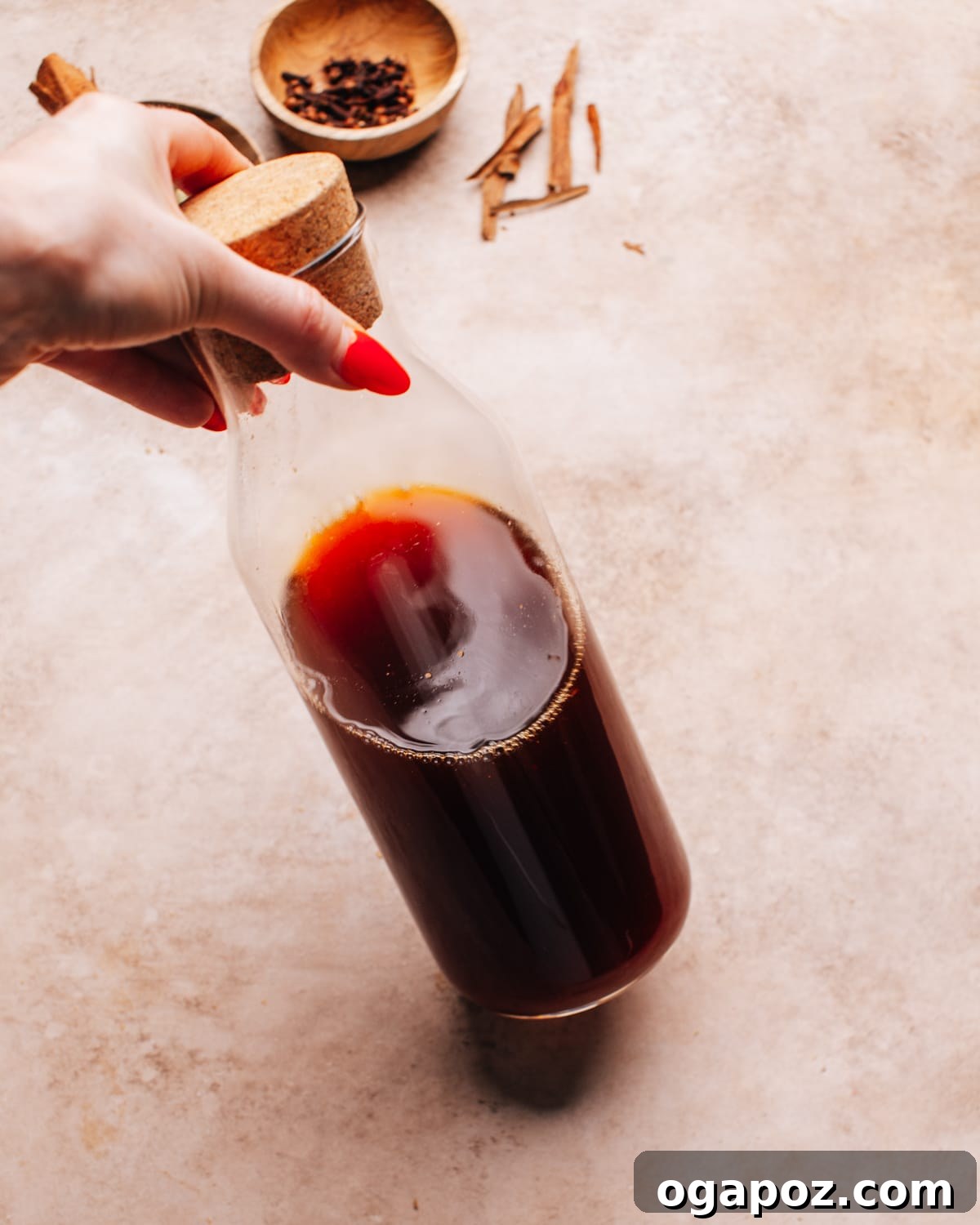 Authentic Chai Concentrate for the Best Homemade Lattes 11 A hand tilting a glass bottle of rich, homemade chai latte concentrate, emphasizing its dark, flavorful essence.