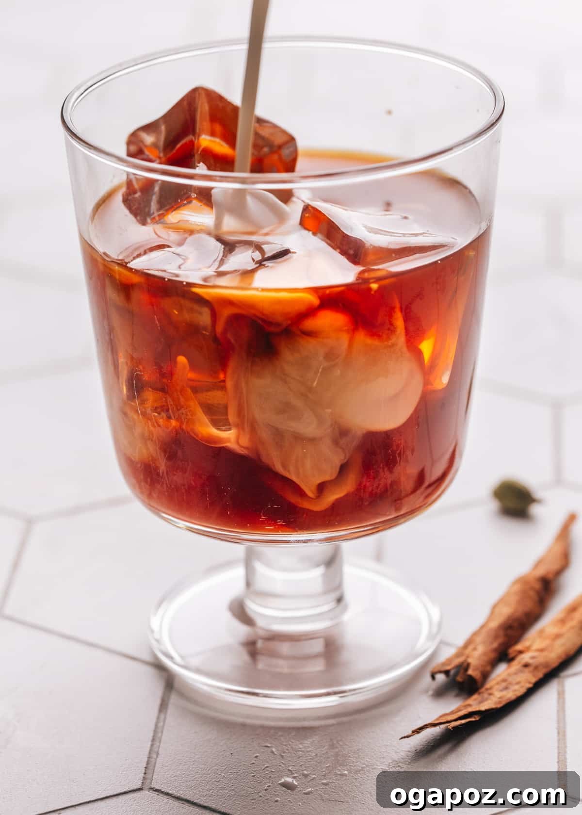 Authentic Chai Concentrate for the Best Homemade Lattes 12 A glass of iced chai latte with milk being poured in, creating a beautiful swirl of contrasting colors, garnished with a cinnamon stick.