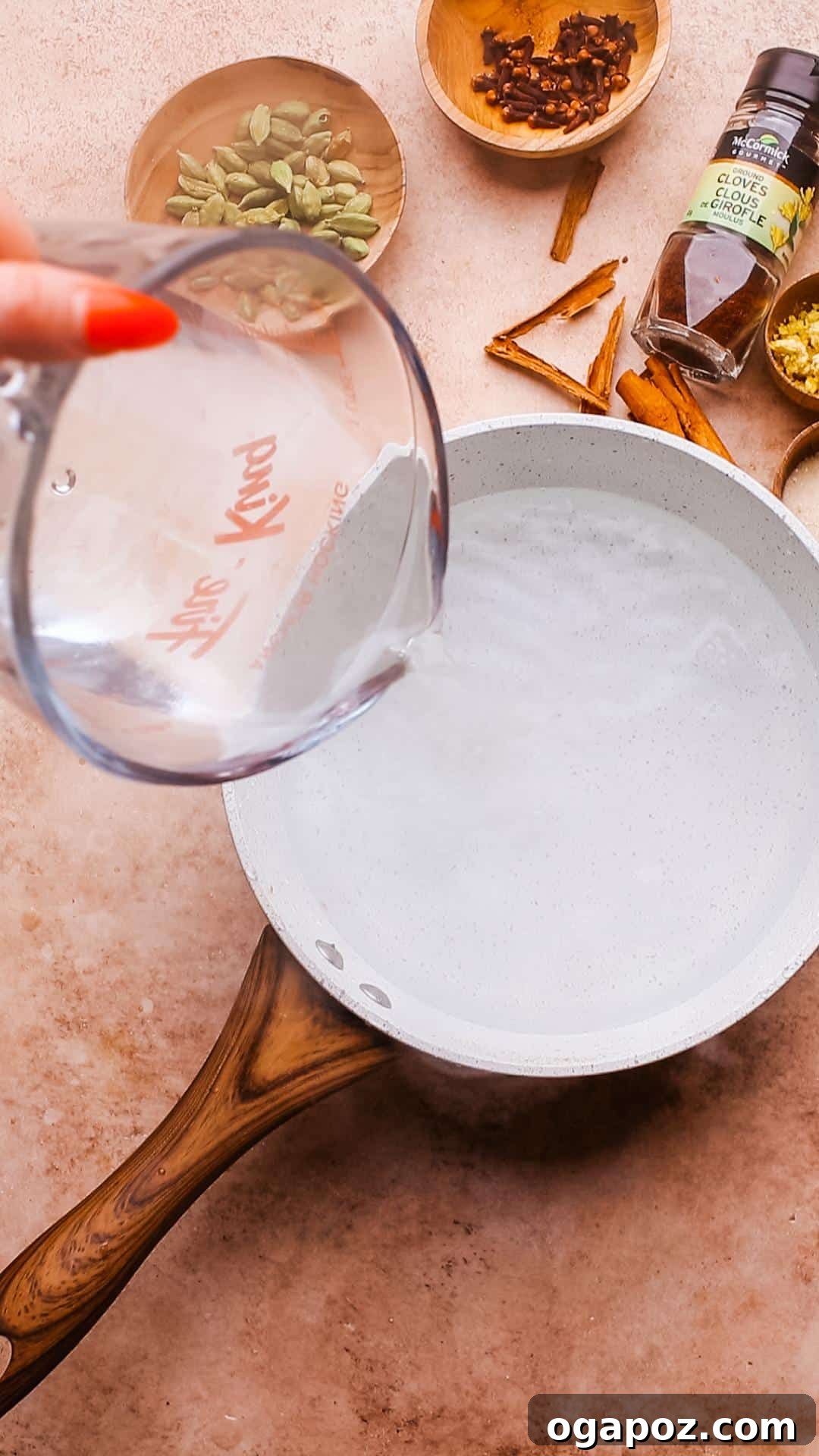 Authentic Chai Concentrate for the Best Homemade Lattes 4 A hand pouring water into a pot on a stovetop, with spices already in the pot, beginning the chai concentrate preparation process.