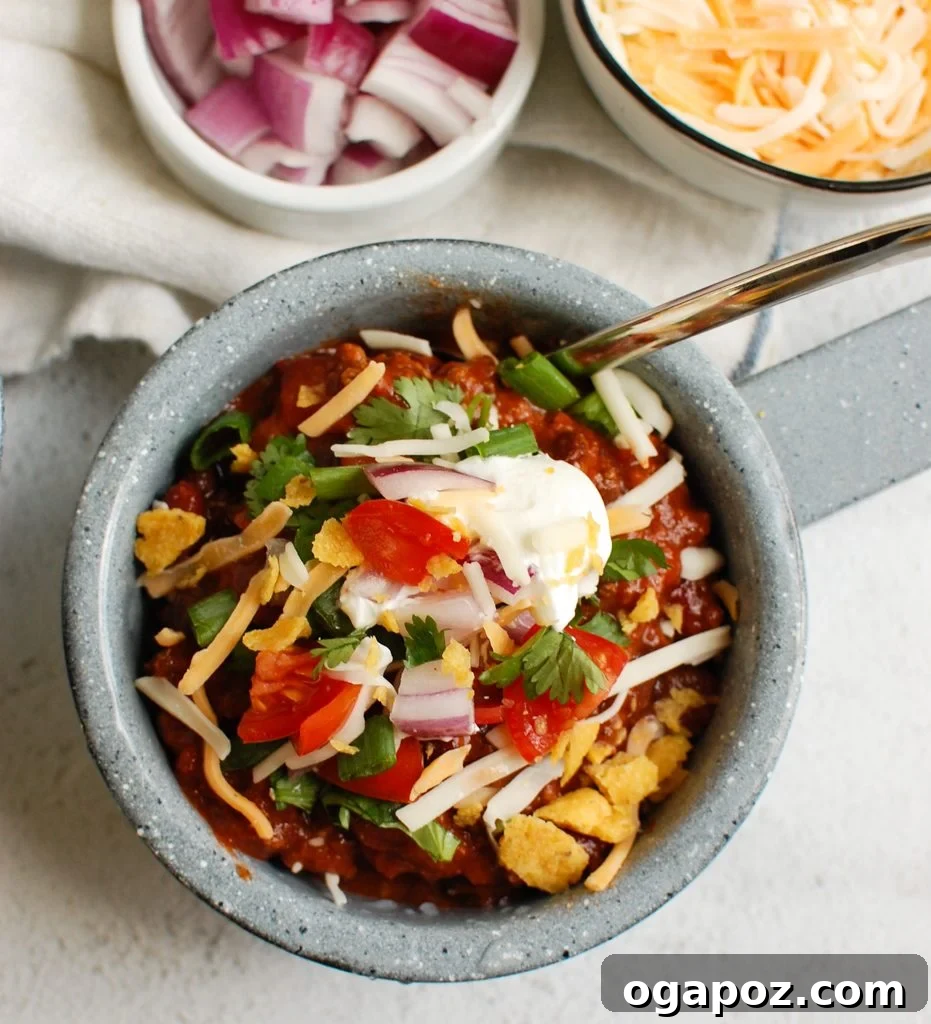 Close-up shot of classic beef chili in a blue bowl with a spoon, highlighting the rich texture and vibrant ingredients.