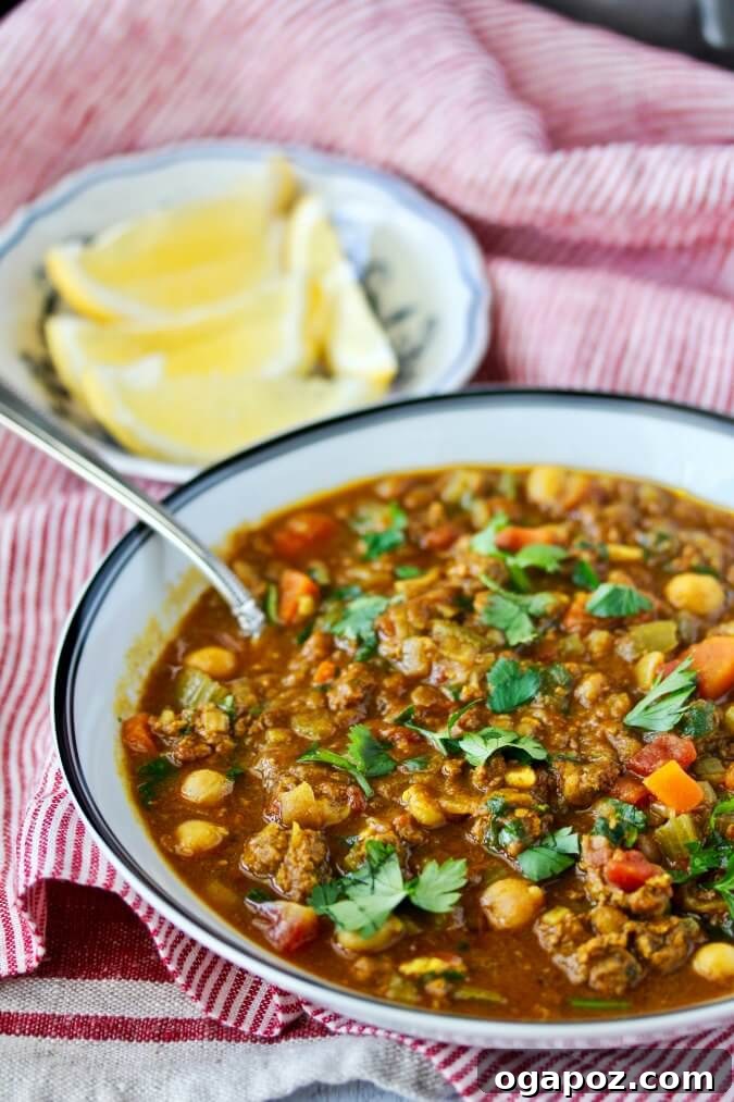 A rich bowl of Moroccan Lamb, Chickpea, and Lentil Soup, known as Harira, garnished with fresh cilantro and a lemon wedge.