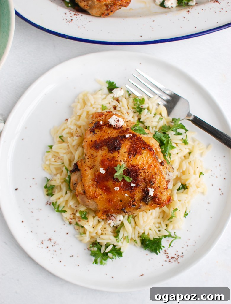 A close-up view of a large platter of cooked Mediterranean Chicken, garnished with fresh herbs and a slice of lemon.
