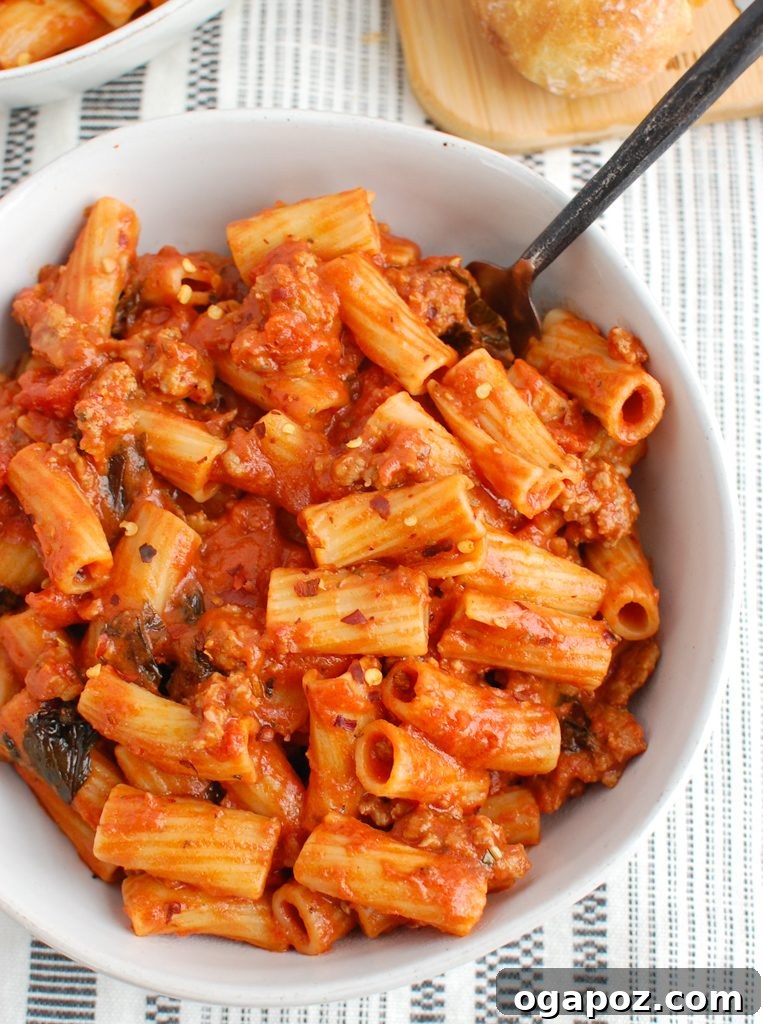 Robust Italian Sausage Pasta 2 A large white bowl filled with creamy Italian Sausage Pasta, garnished with fresh basil leaves and grated Parmesan cheese, ready to be enjoyed.