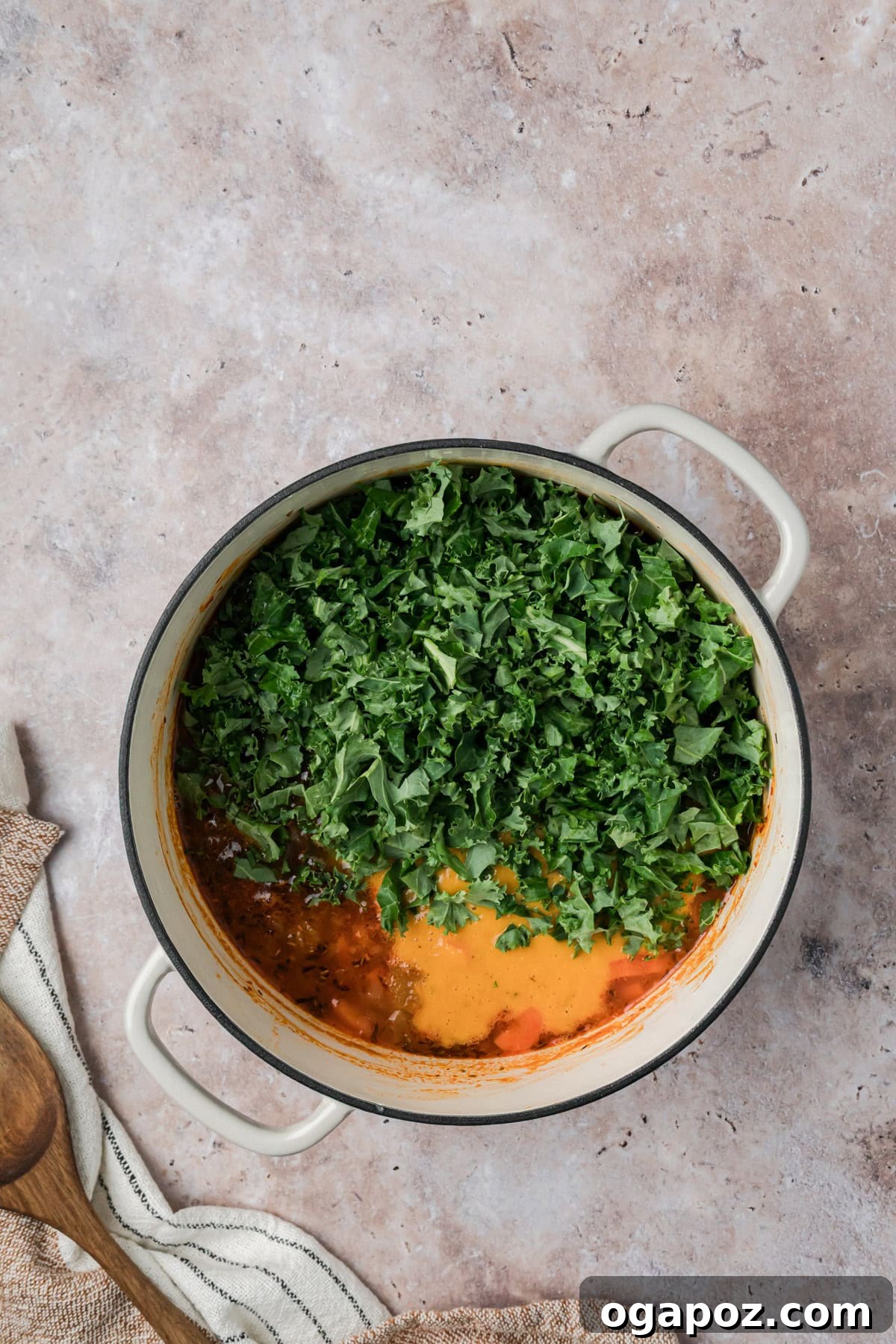 Freshly chopped kale being stirred into the simmering Tuscan white bean soup, wilting beautifully into the rich and aromatic broth, ready for the final touches.