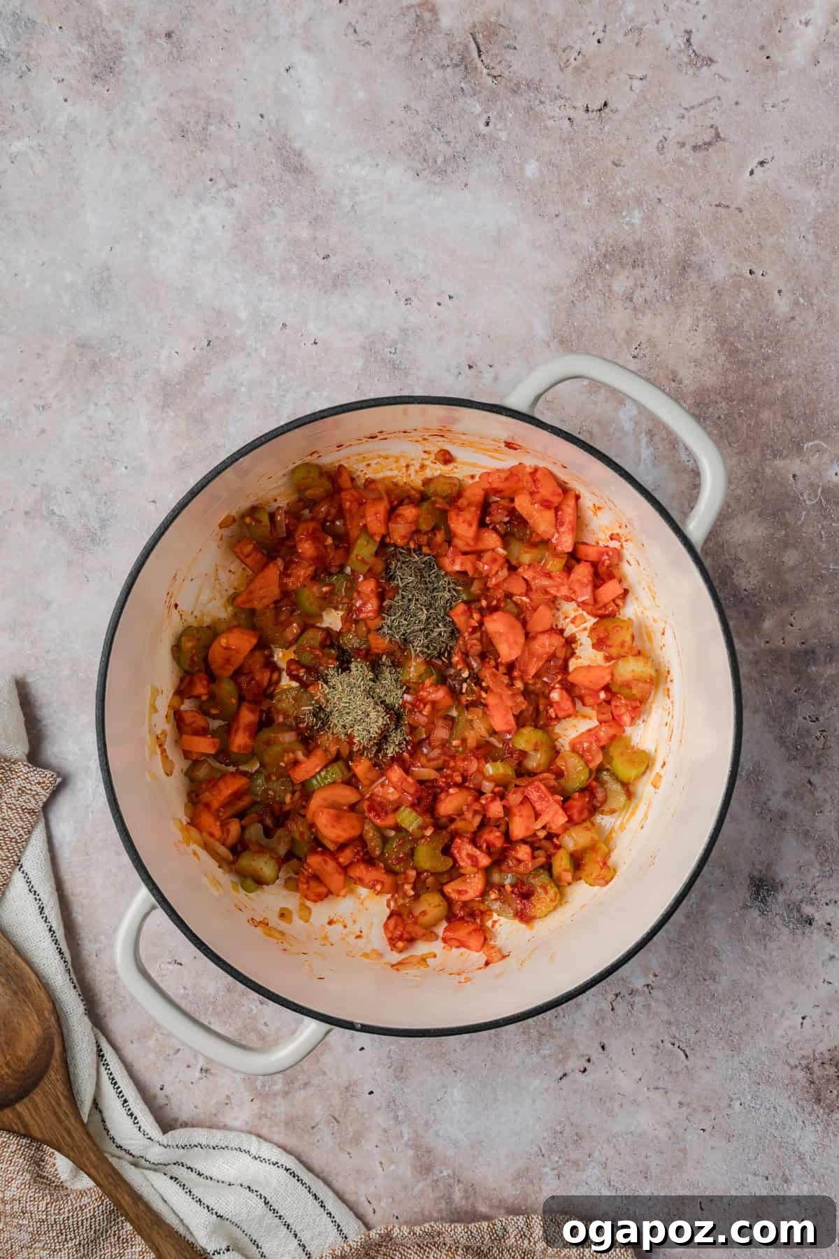 Minced garlic, tomato paste, and a blend of dried thyme, rosemary, and red pepper flakes being stirred into the sautéed vegetables in a pot, infusing the Tuscan White Bean Soup with rich aromas and depth of flavor.