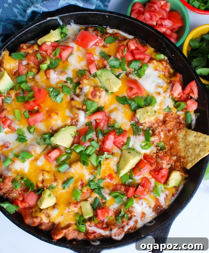 Party Perfect Beef Taco Dip 2 Delicious Beef Taco Dip served hot in a skillet, garnished with fresh cilantro and green onions, ready to be scooped with tortilla chips.