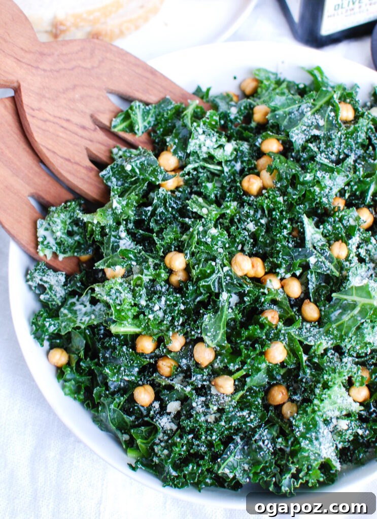 Elevated Kale Caesar 3 Close-up of Kale Caesar Salad with wood tongs, showing crispy chickpeas and Parmesan.