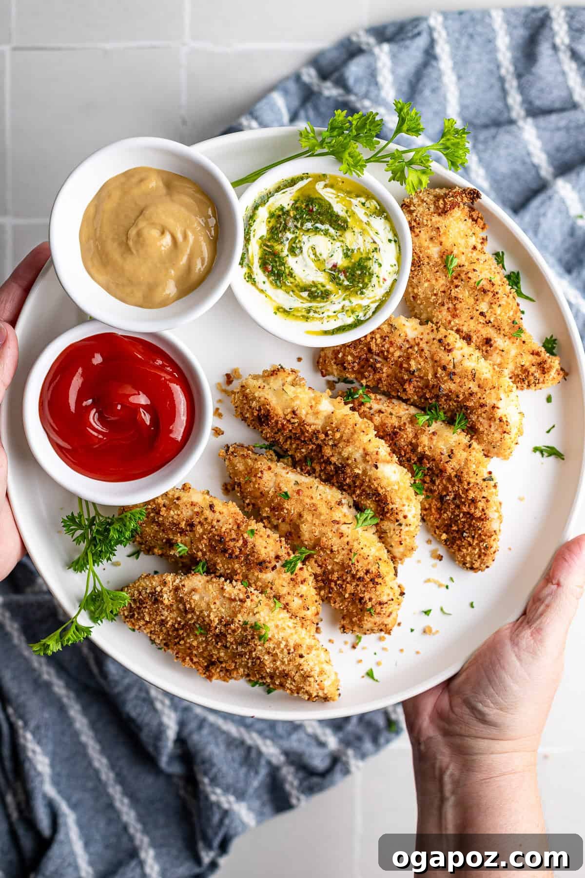 Golden Crispy Oven Baked Chicken Tenders 2 Crispy baked chicken fingers on a white plate, golden brown and ready to serve with three dipping sauces.