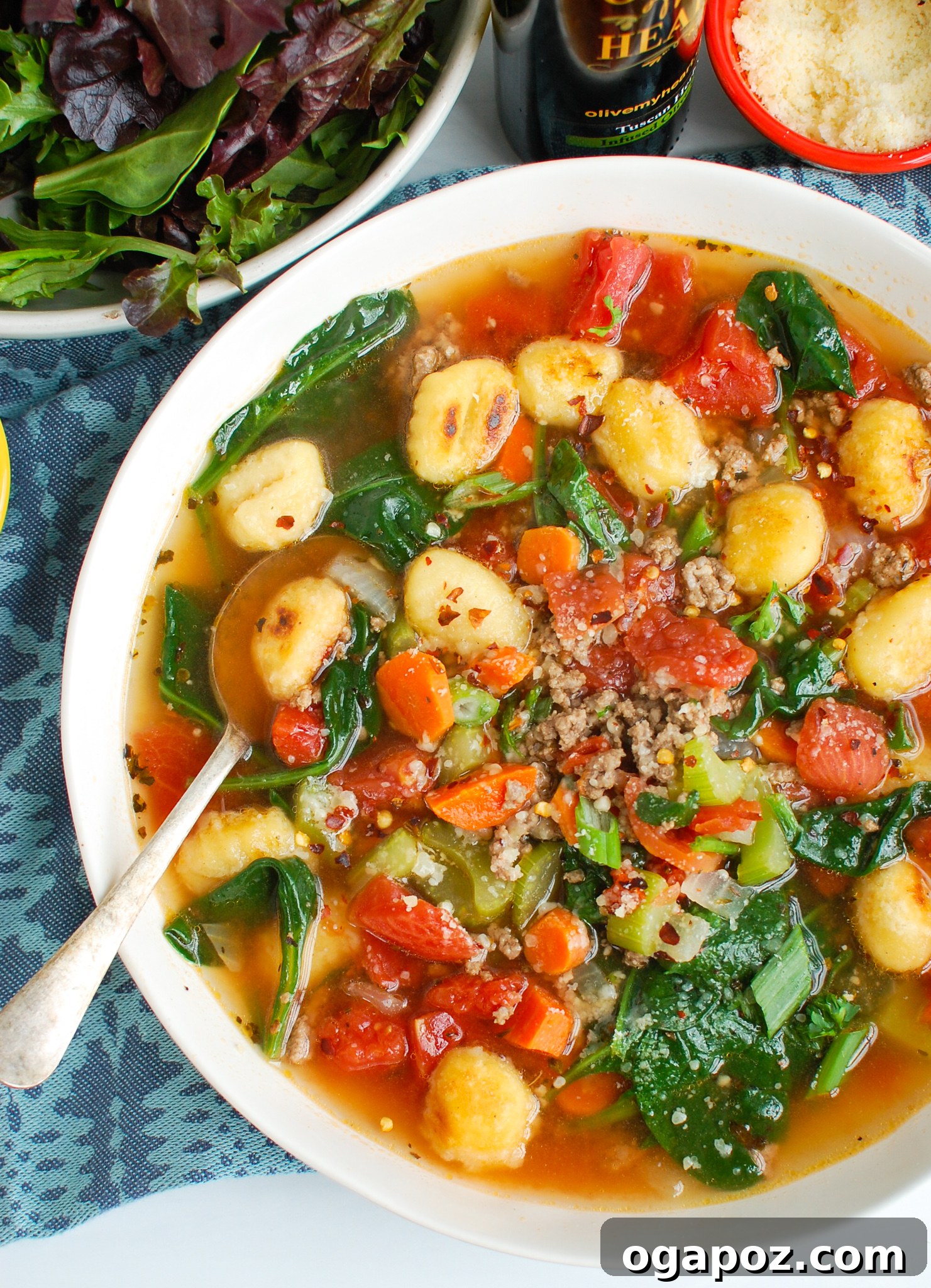 A bowl of Easy Sausage Gnocchi Soup placed next to a blue napkin on a rustic wooden table.