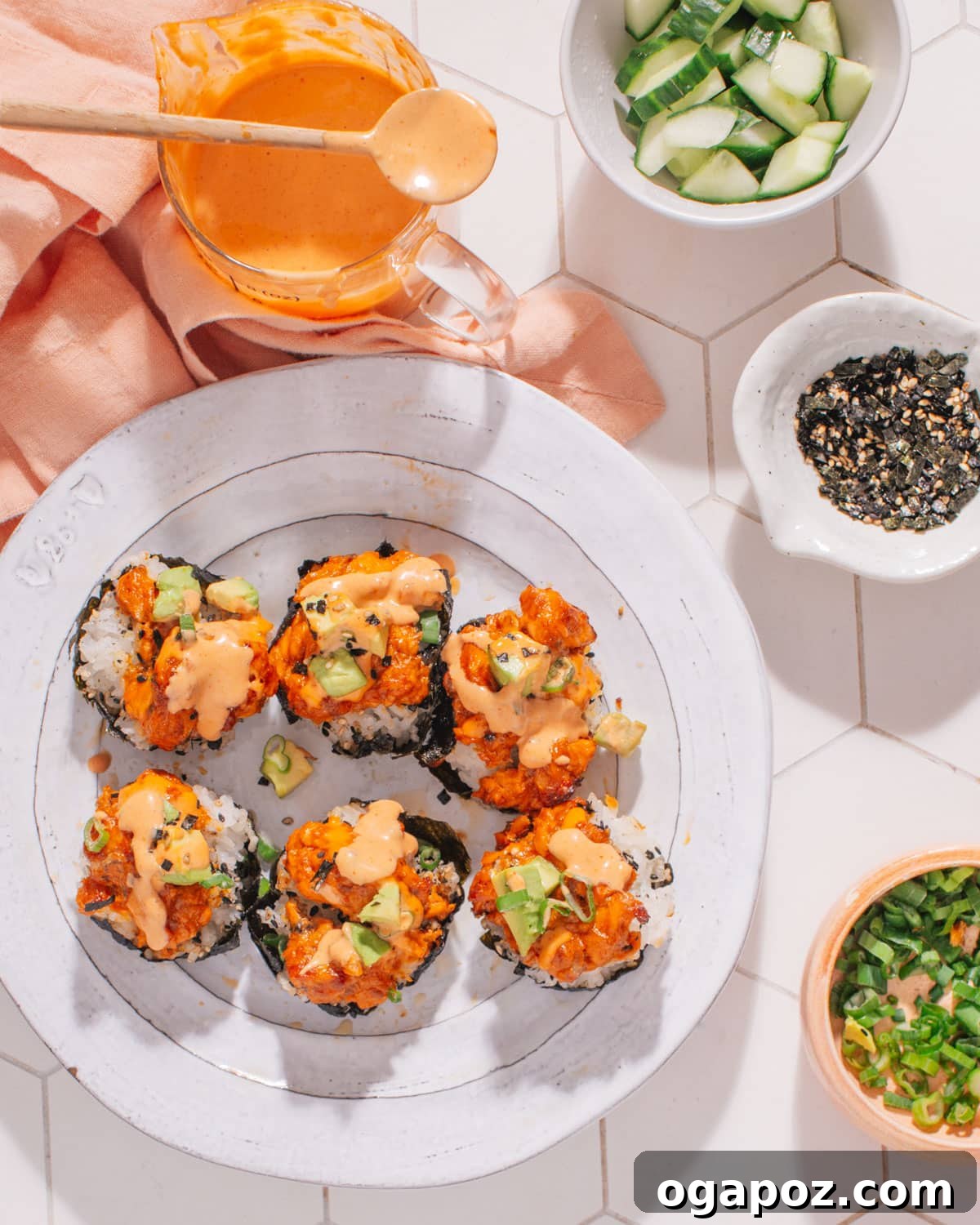 A close-up of several baked salmon rice muffins garnished with spicy mayo, green onions, and sesame seeds, on a serving platter.