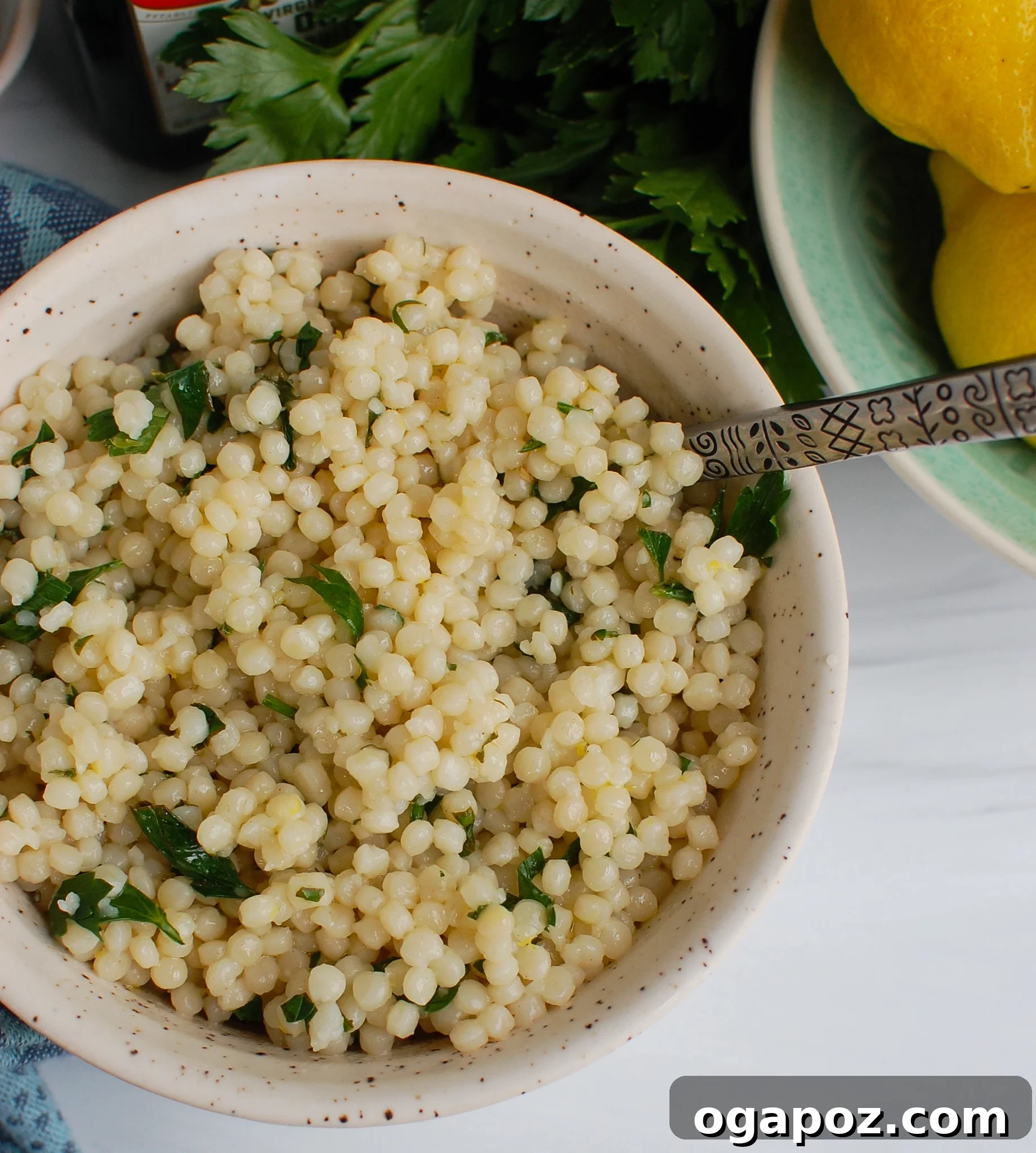 Sunshine Lemon Pearl Couscous 4 A wooden spoon scooping Lemon Pearl Couscous from a white bowl, showing its texture and herb flecks.