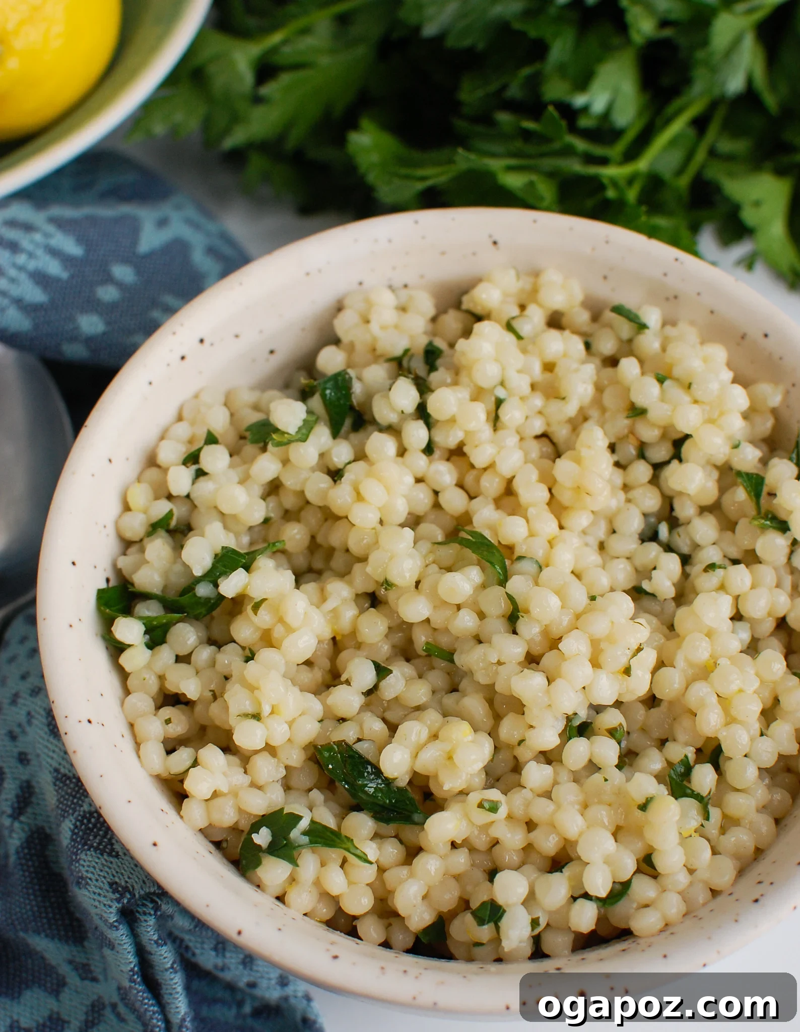 Sunshine Lemon Pearl Couscous 6 A white bowl of Lemon Pearl Couscous placed on a rustic napkin with a fork, ready to be served.