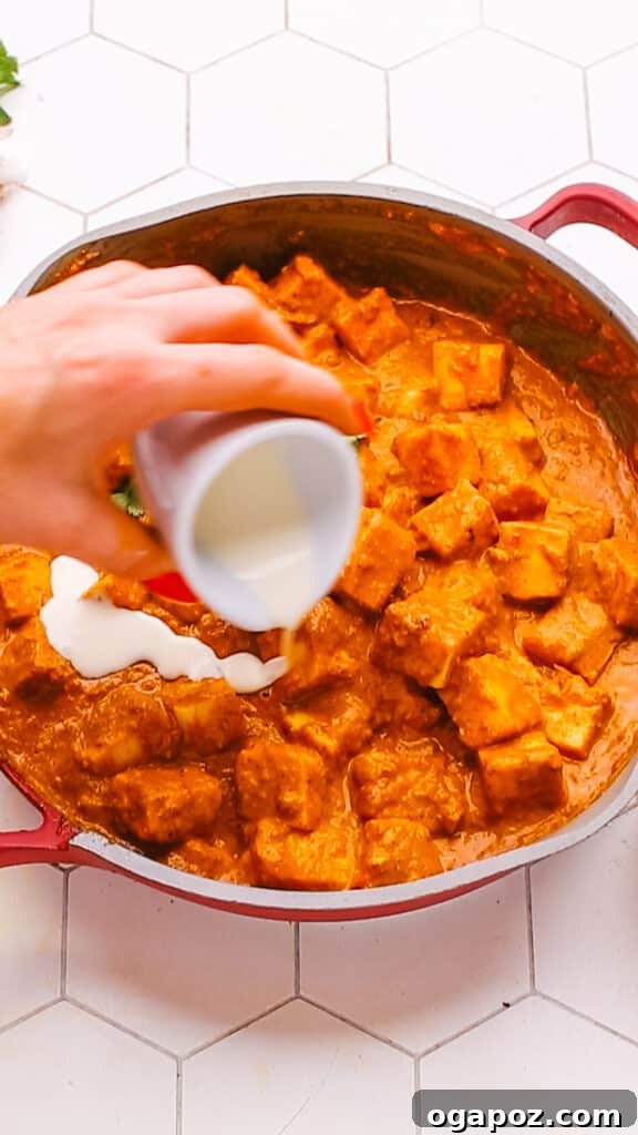 Creamy Butter Paneer 16 Drizzling heavy cream over a freshly prepared bowl of rich Butter Paneer Masala, ready to serve.