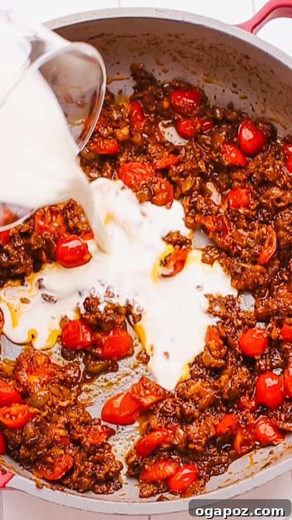 Creamy Butter Paneer 10 Diced tomatoes and rich heavy cream being gently stirred into the fragrant Butter Paneer sauce in a pan.