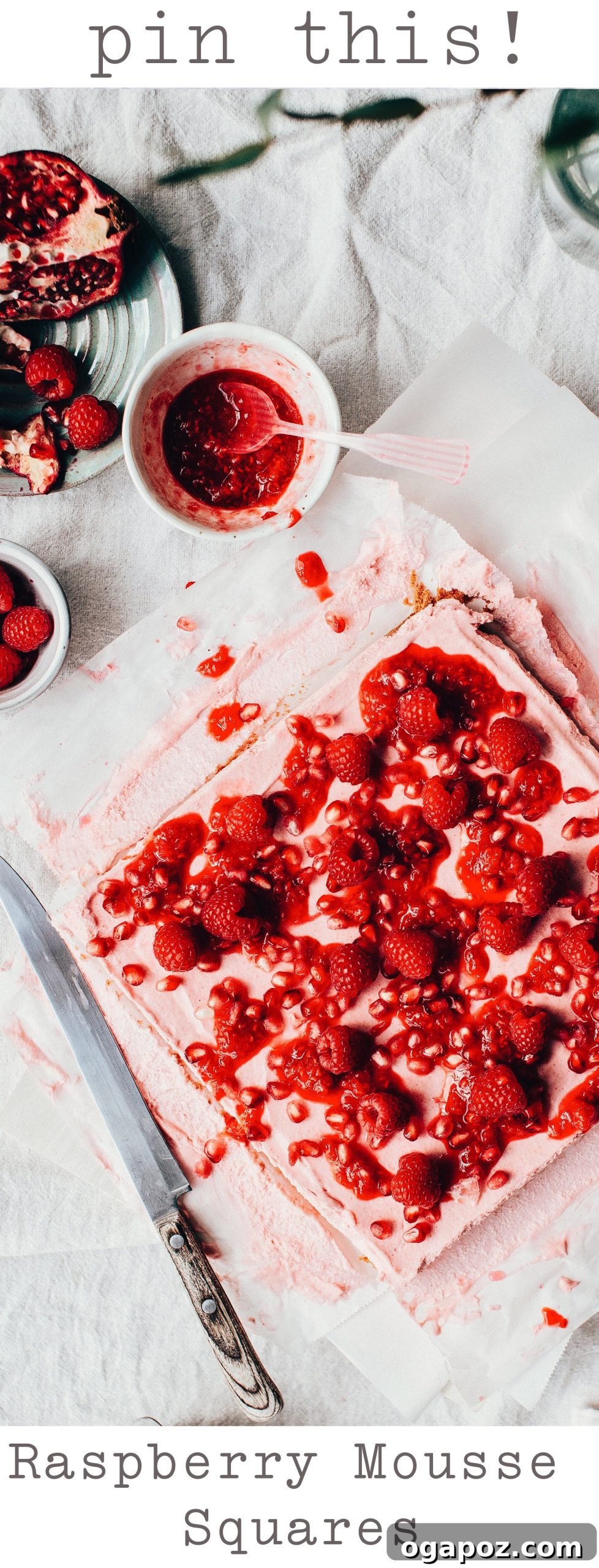Luscious Raspberry Mousse Squares 12 Artfully arranged Raspberry Mousse Squares with additional fresh berries and pomegranate arils on a textured surface.