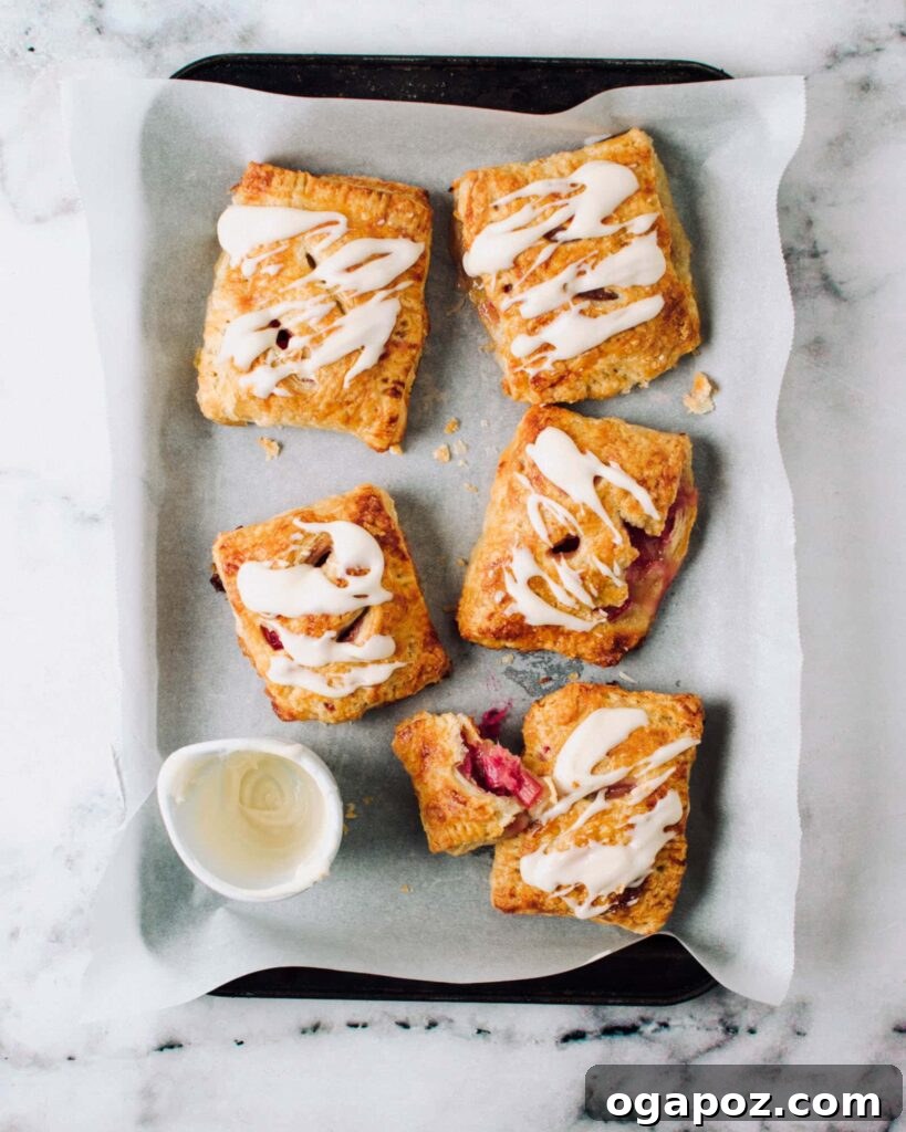 Our Go-To Easy Rhubarb Recipes 15 Several rhubarb hand pies on a baking tray, featuring a lovely white glaze and perfectly flaky handmade pastry.