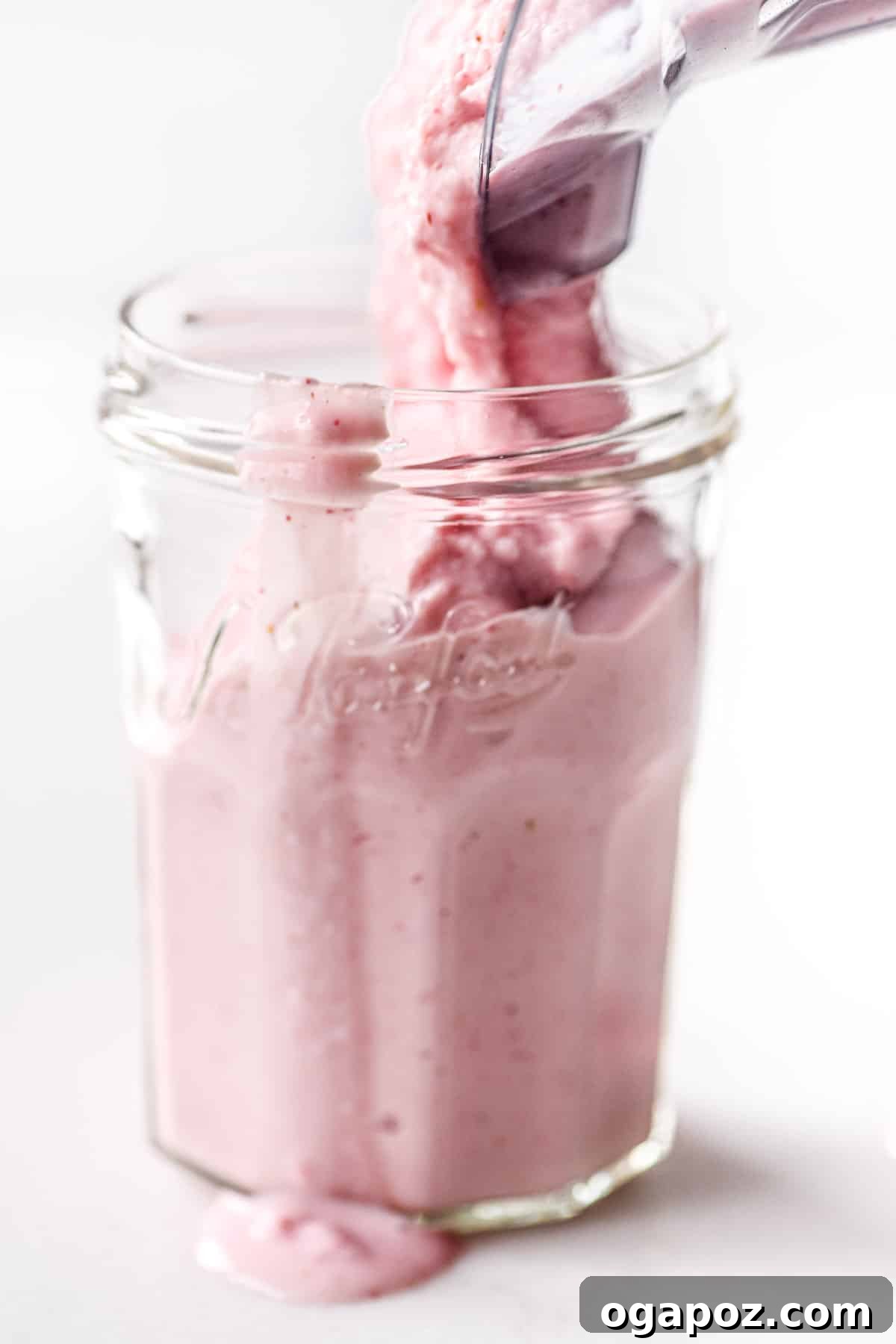 Our Go-To Easy Rhubarb Recipes 23 A vibrant pink rhubarb smoothie in a tall glass, garnished with fresh fruit and a mint leaf.