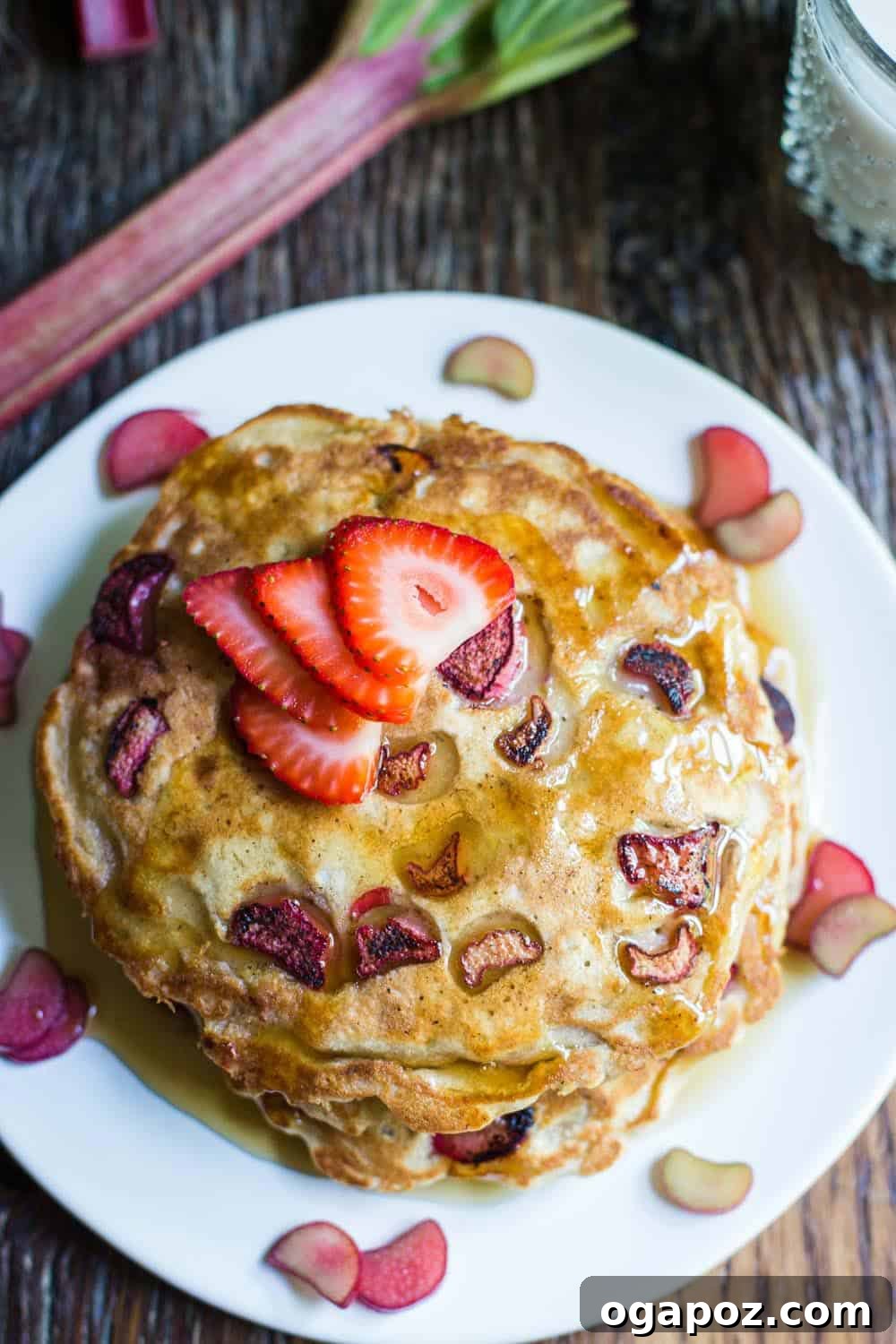 Our Go-To Easy Rhubarb Recipes 24 Stacks of fluffy rhubarb pancakes with diced rhubarb pieces visible, drizzled with maple syrup.