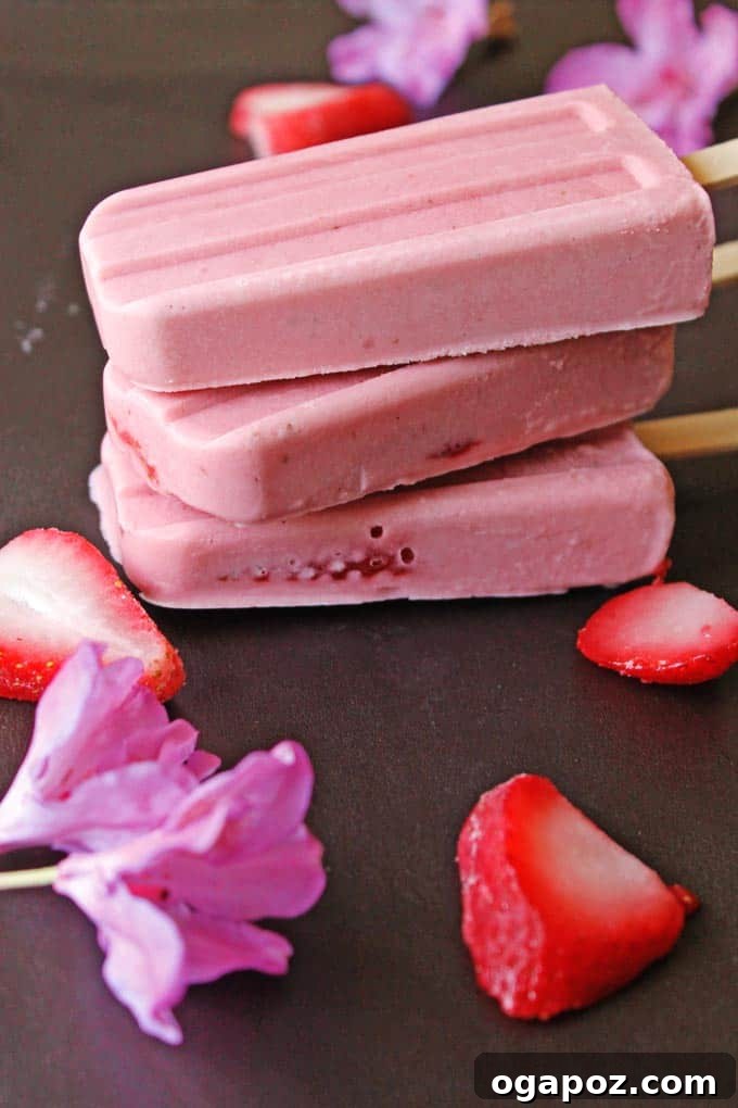 Our Go-To Easy Rhubarb Recipes 25 Homemade rhubarb and strawberry popsicles with a natural pink hue, arranged enticingly on a wooden tray.