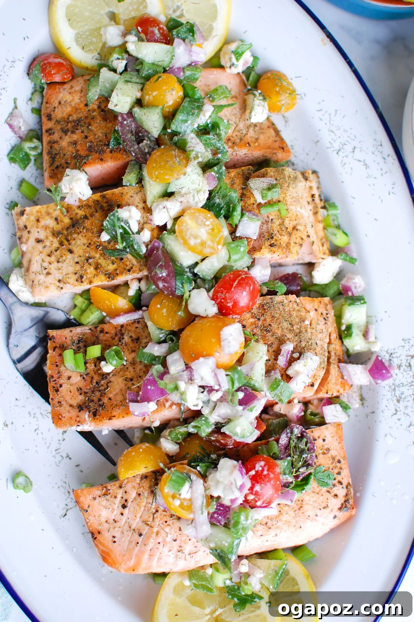 Sun-Kissed Mediterranean Baked Salmon 6 Mediterranean Salmon on white platter topped with fresh tomatoes, feta cheese, and herbs.