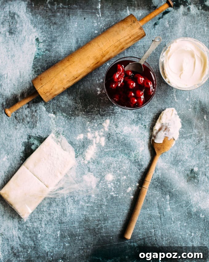Almond-Kissed Cherry Cheese Turnovers 3 Ingredients laid out for Cherry Cheese Turnovers: puff pastry sheets, a bowl of cherry pie filling, and softened cream cheese