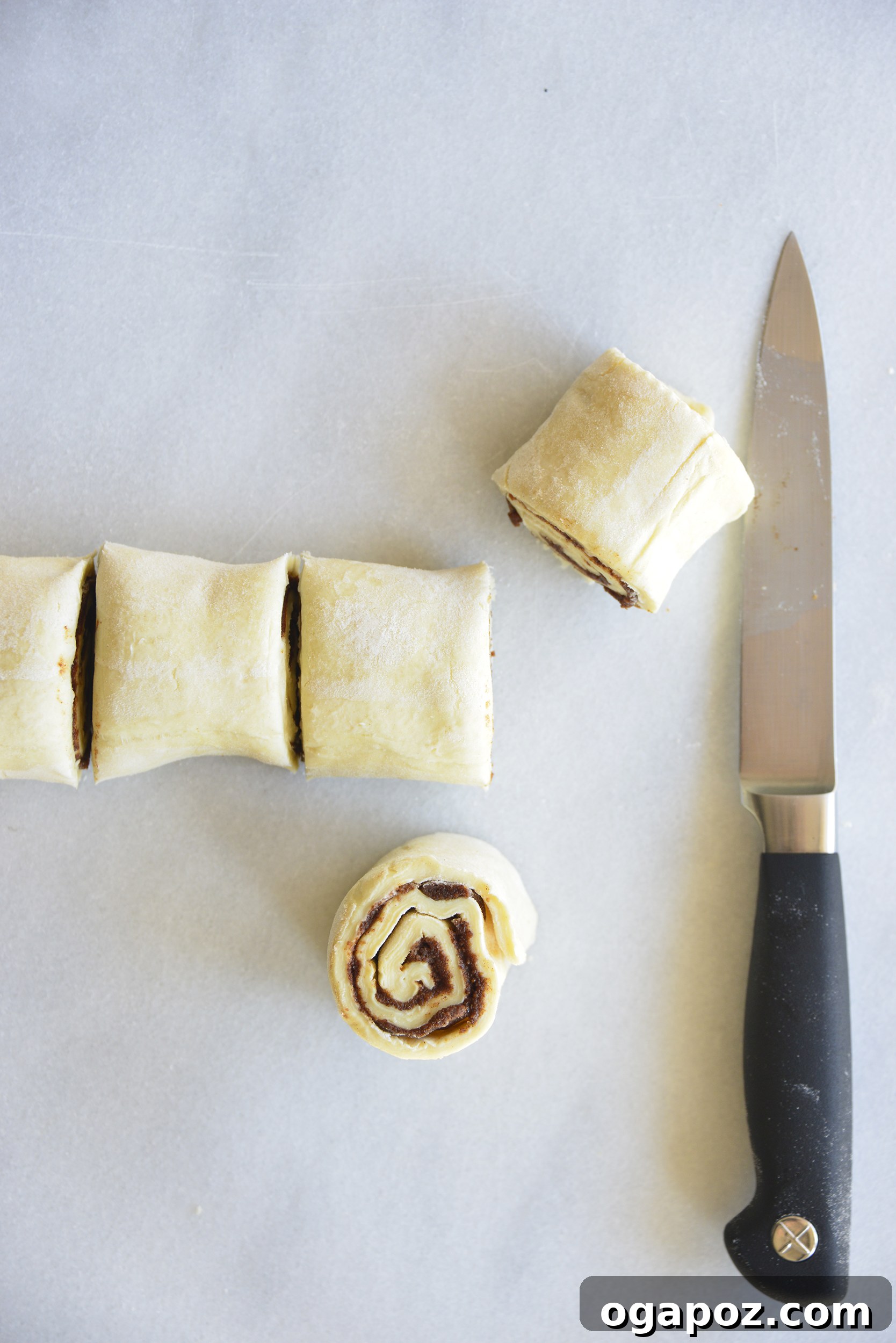Effortless Cinnamon Puff Pastry Swirls 7 The rolled puff pastry log, expertly sliced into six uniform cinnamon swirls, resting on parchment paper.