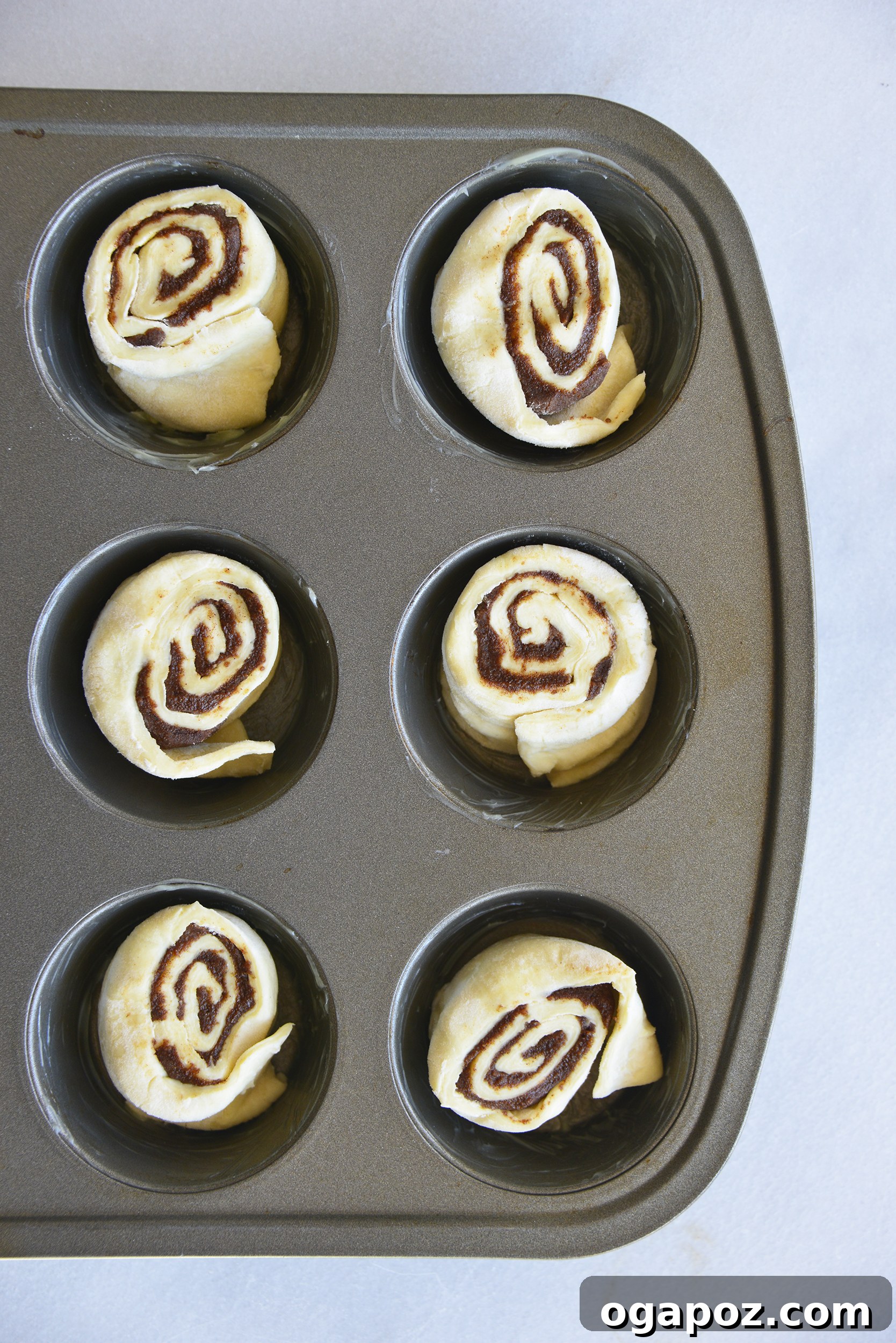 Effortless Cinnamon Puff Pastry Swirls 8 Puff pastry cinnamon swirls nestled in a muffin tin, arranged neatly and awaiting baking.