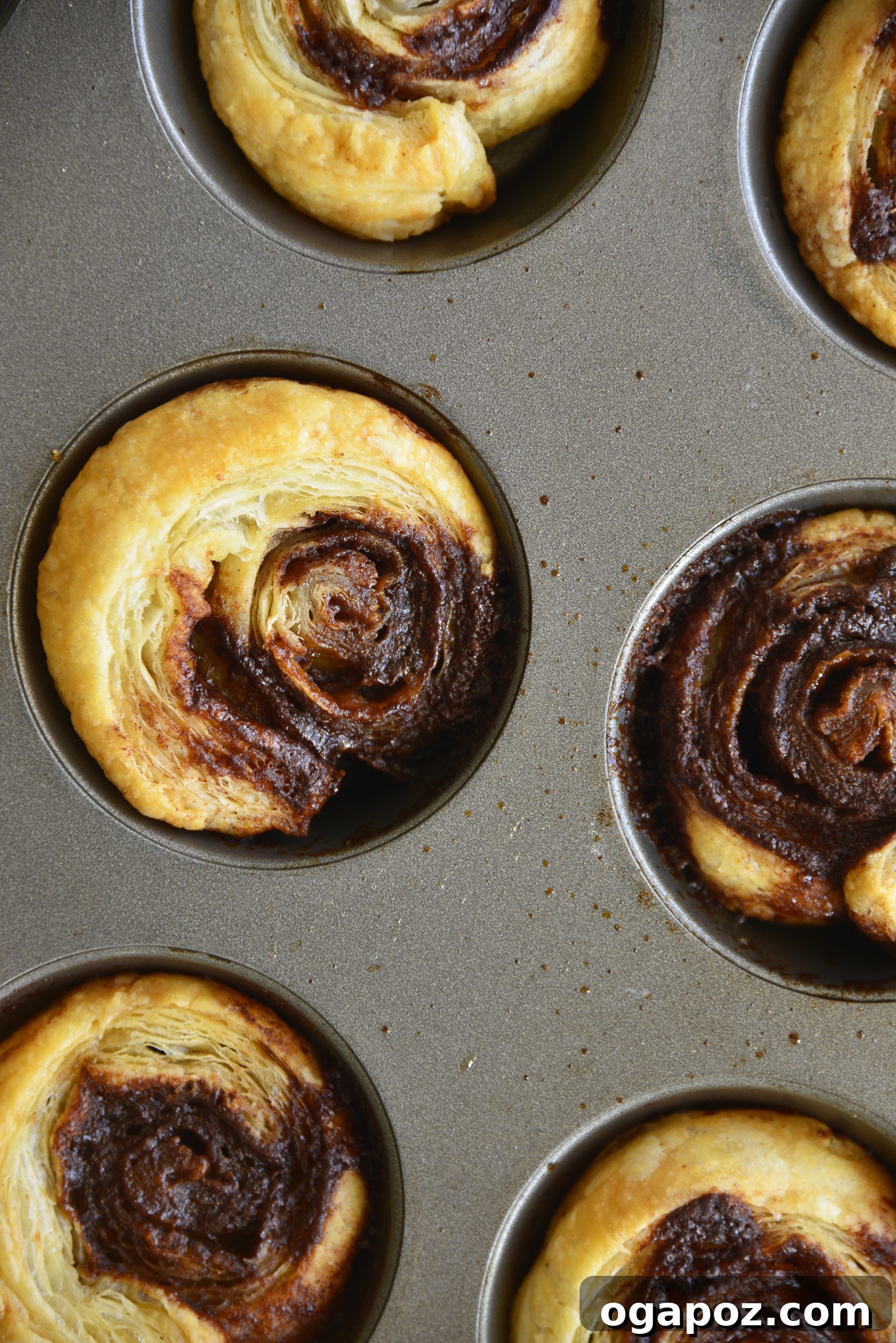 Effortless Cinnamon Puff Pastry Swirls 9 Freshly baked Easy Puff Pastry Cinnamon Swirls still in the muffin tin, exhibiting their irresistible golden-brown color and fluffy texture.