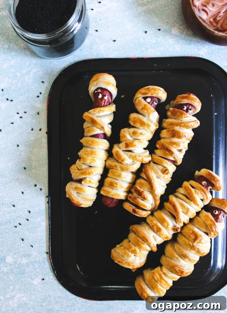 Spooky Sausage Wraps 2 Mummy Hot Dogs on a black plate, ready to be enjoyed as a spooky Halloween snack.