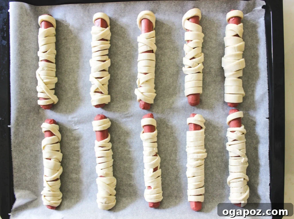 Spooky Sausage Wraps 5 Close-up of hot dogs being wrapped with puff pastry strips to create the mummy effect.