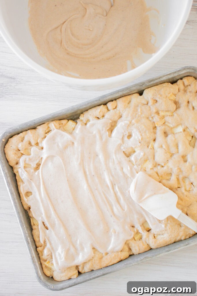 Autumn Apple Bars with Pumpkin Spice Glaze 7 A generous layer of creamy pumpkin pie spice icing being smoothly spread over the cooled apple bars using a spatula, creating an even topping.