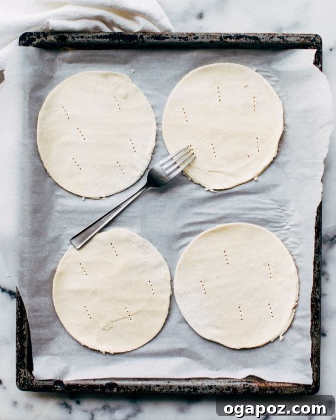 Effortless Flaky Samosas 6 Step-by-step image showing how to scoop the spiced potato and pea filling onto puff pastry half-circles and fold them into samosa shapes.