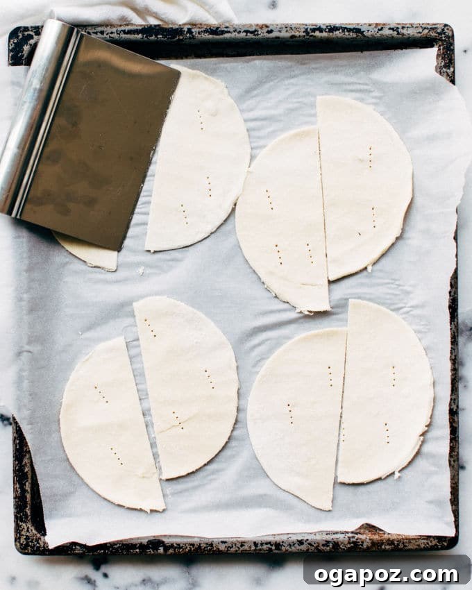 Effortless Flaky Samosas 7 Puff pastry circles cut in half and pricked with a fork, laid out on parchment paper, ready for filling to make delicious baked samosas.
