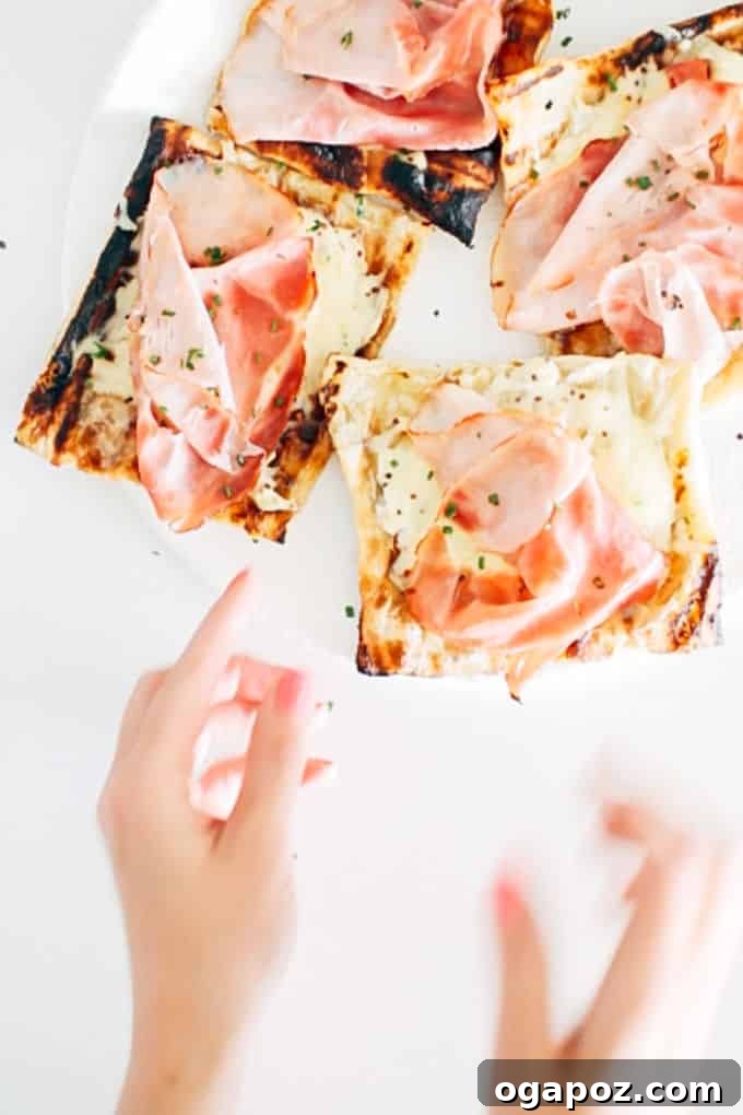 Flaky Grilled Ham and Gruyere Pastries 2 Golden brown grilled puff pastry ham and gruyere tarts on a grilling grate, topped with melted cheese, ham, and fresh chives, ready to serve.